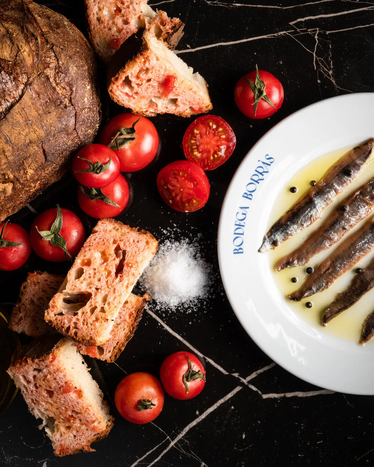 Anchovies, bread and tomatoes on black marble