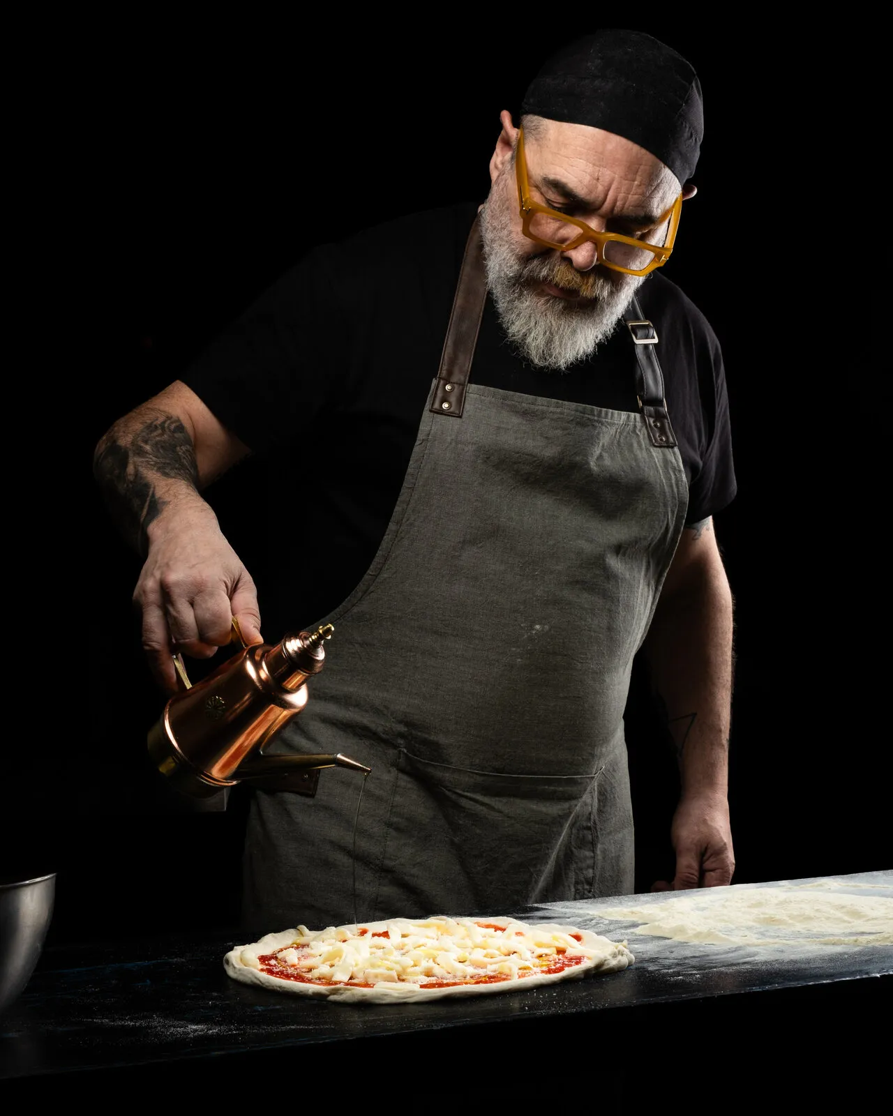 Pizza maker dressing a freshly baked pizza